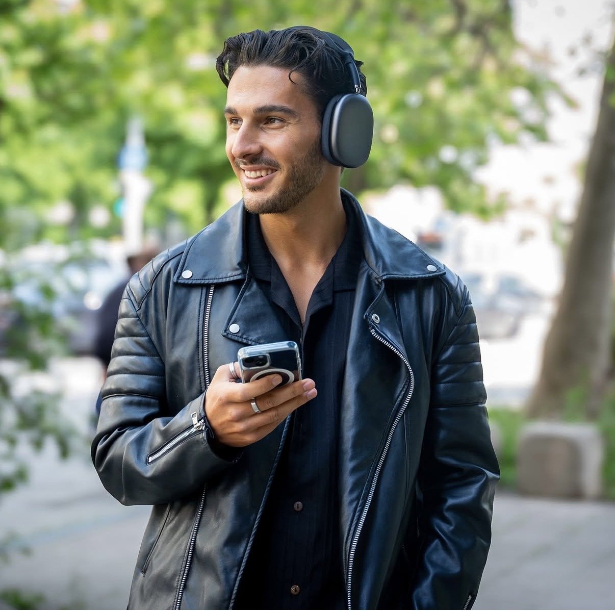 Frederic in Lederjacke mit Kopfhörern und Smartphone in der Stadt