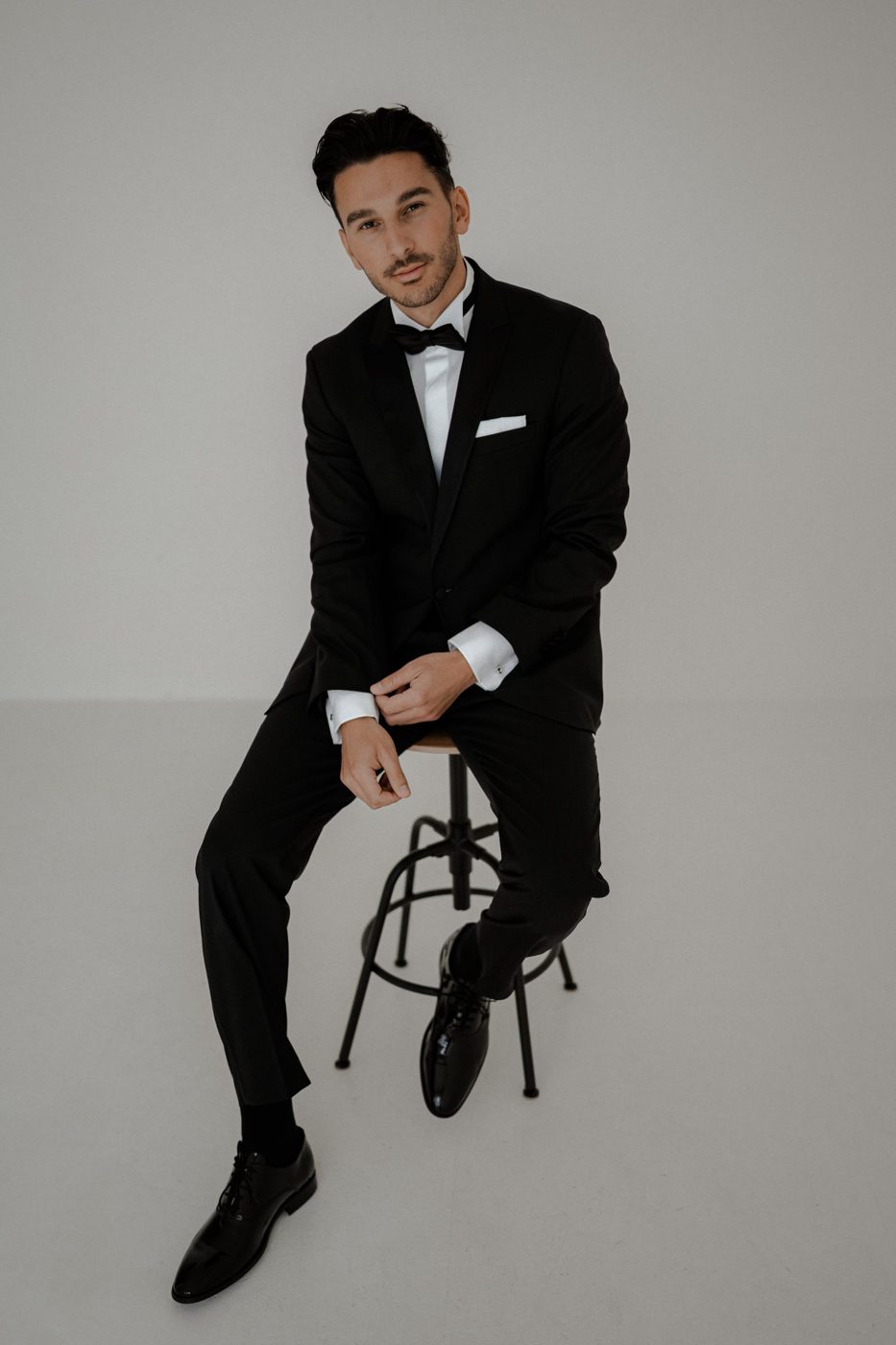 Frederic im schwarzen Smoking mit Fliege auf einem Hocker im Fotostudio